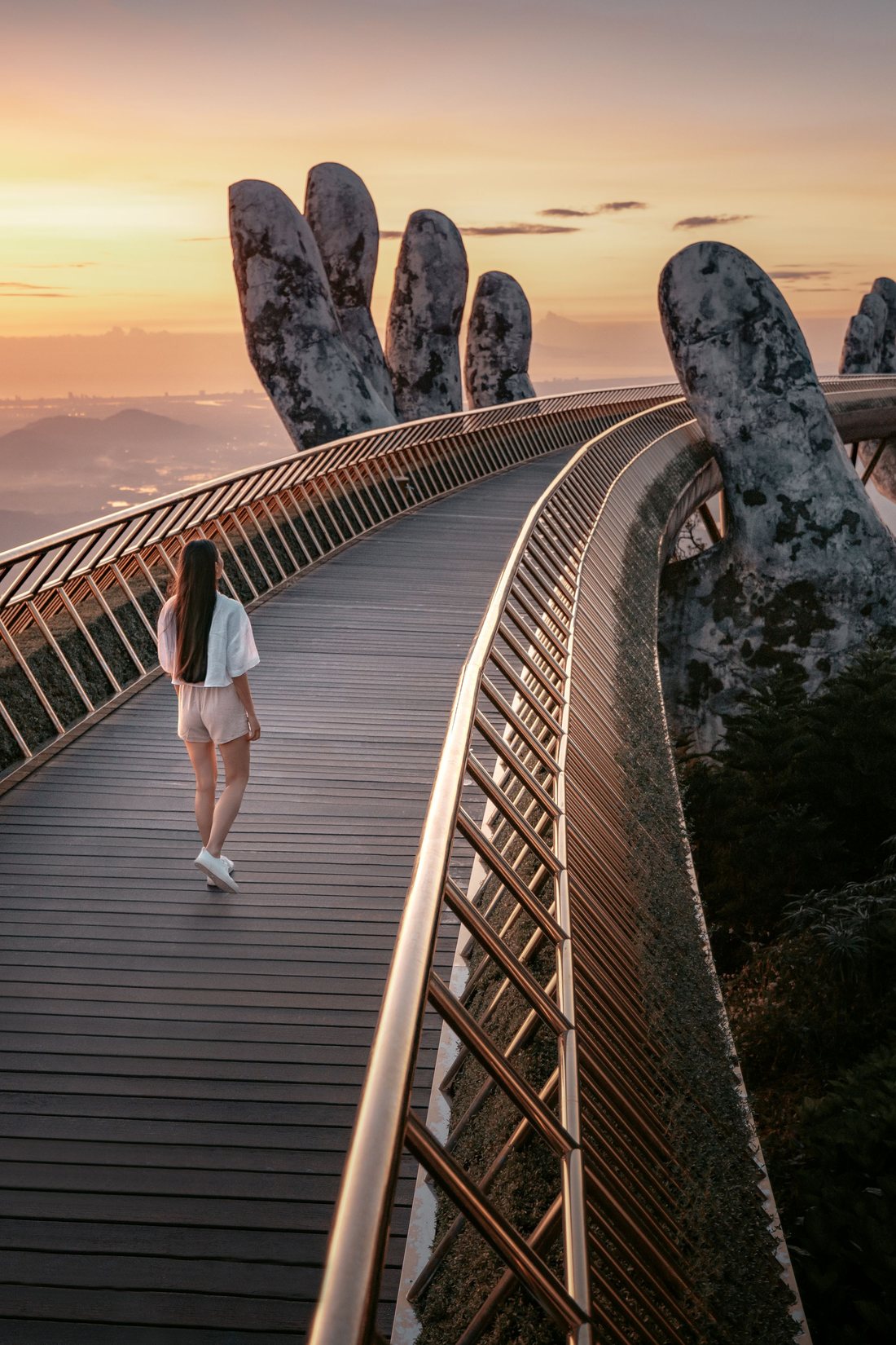 A visitor walking the Golden Bridge at sunrise, held up by two giant stone hands at Ba Na Hills