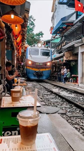 A train passing through Hanoi's Train Street while visitors sip coffee at the track side